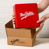 Mrs. Fields signature red tin coming out of a Mrs. Fields branded mailer on a white table top surface.