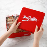 A Mrs. Fields signature red tin being opened to reveal individually sealed cookies on top of a marbled table top surface.