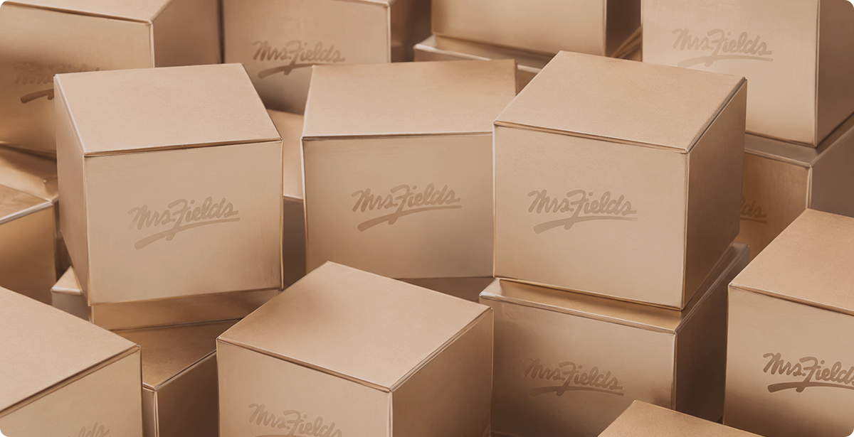 Multiple kraft paper boxes stacked together, each printed with the brand name 'MrsFields' in a cursive script.