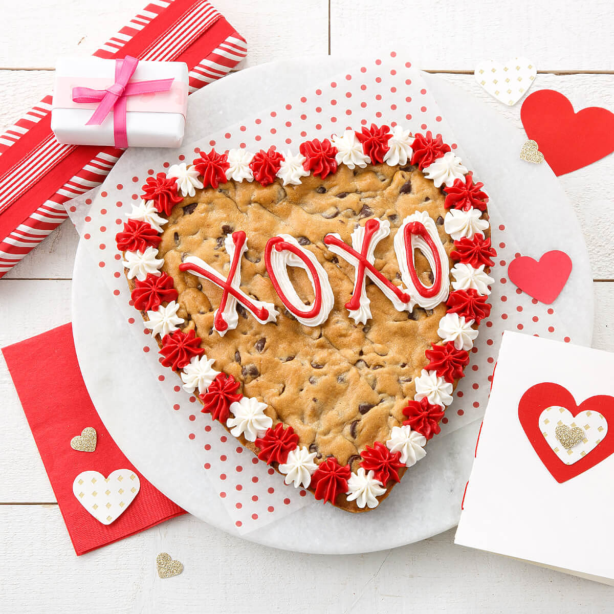 Red and white frosting saying XOXO on a heart shaped cookie cake