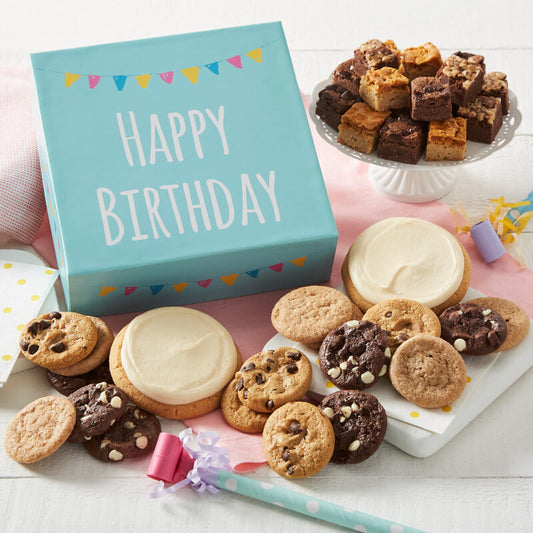 A blue Happy Birthday gift box surrounded by an assortment of nibblers, brownie bites, and two frosted white round cookies