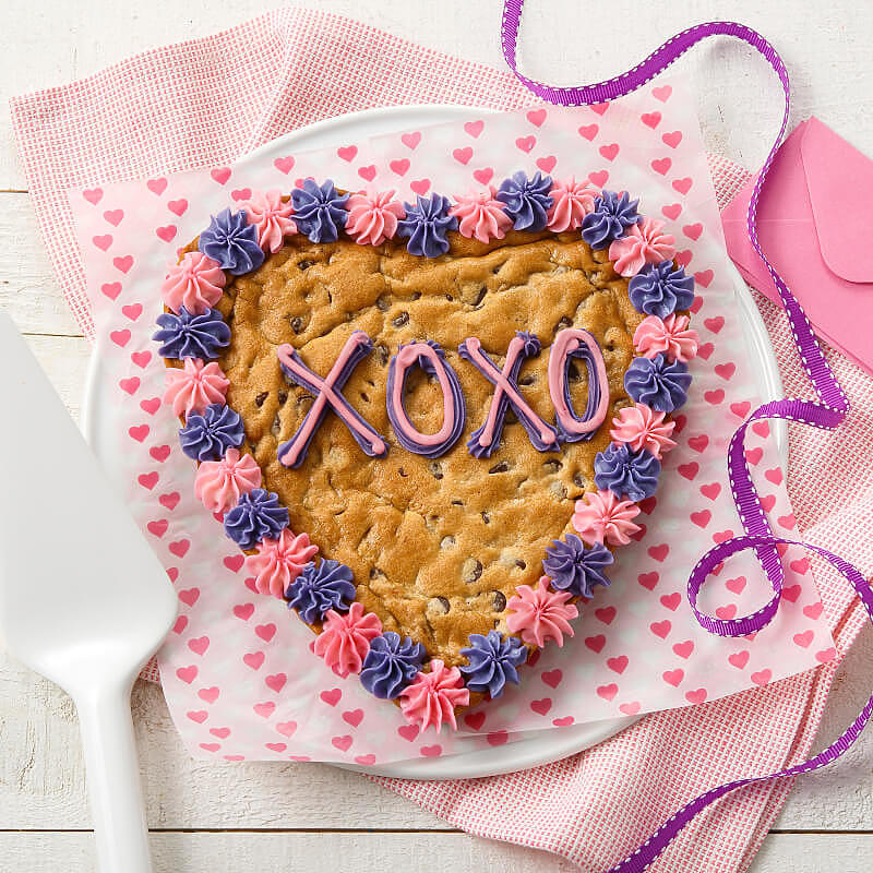 Pink and purple frosting saying XOXO on a heart shaped cookie cake