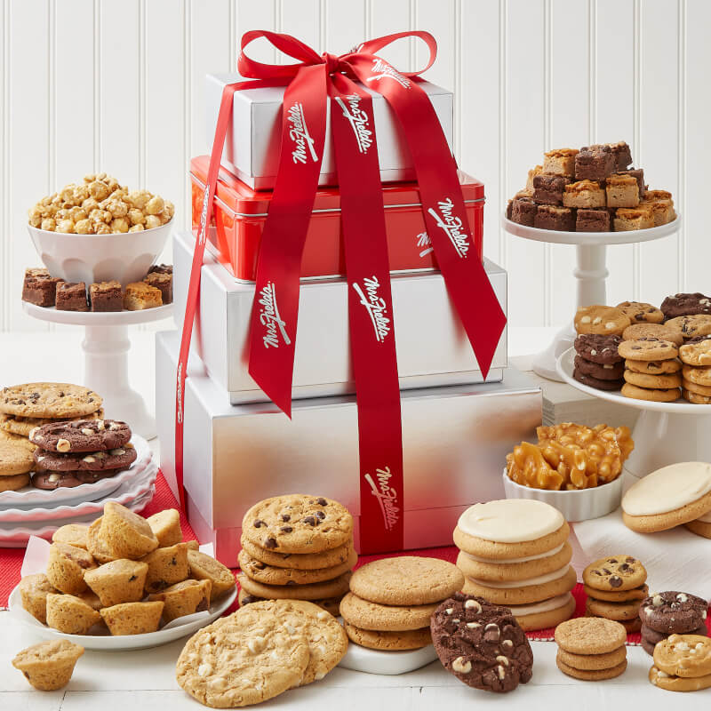 A four tier gift tower surrounded by an assortment of nibblers, original cookies, brownie bites, mini muffins, popcorn, and peanut brittle