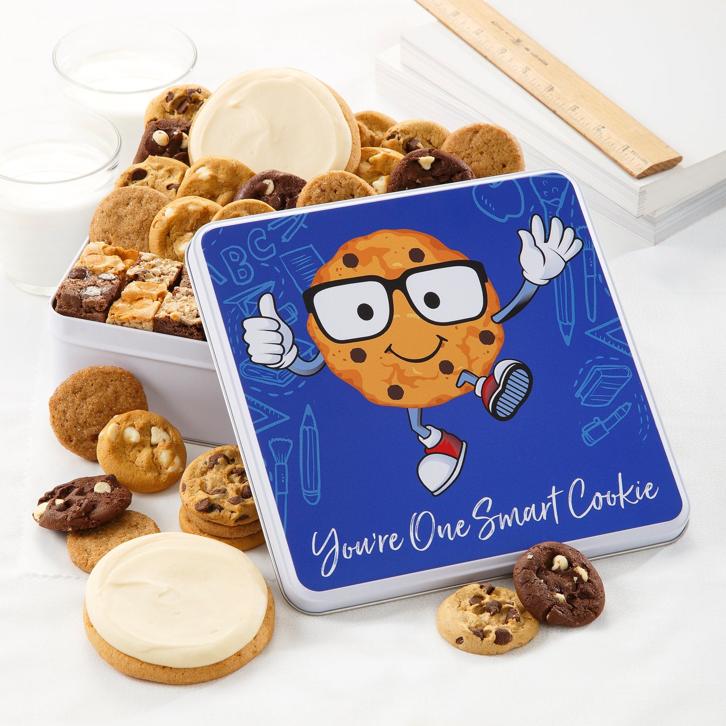 A school-themed gift tin with the sentiment of You're One Smart Cookie filled with an assortment of Nibblers®, brownie bites, and two frosted white round cookies